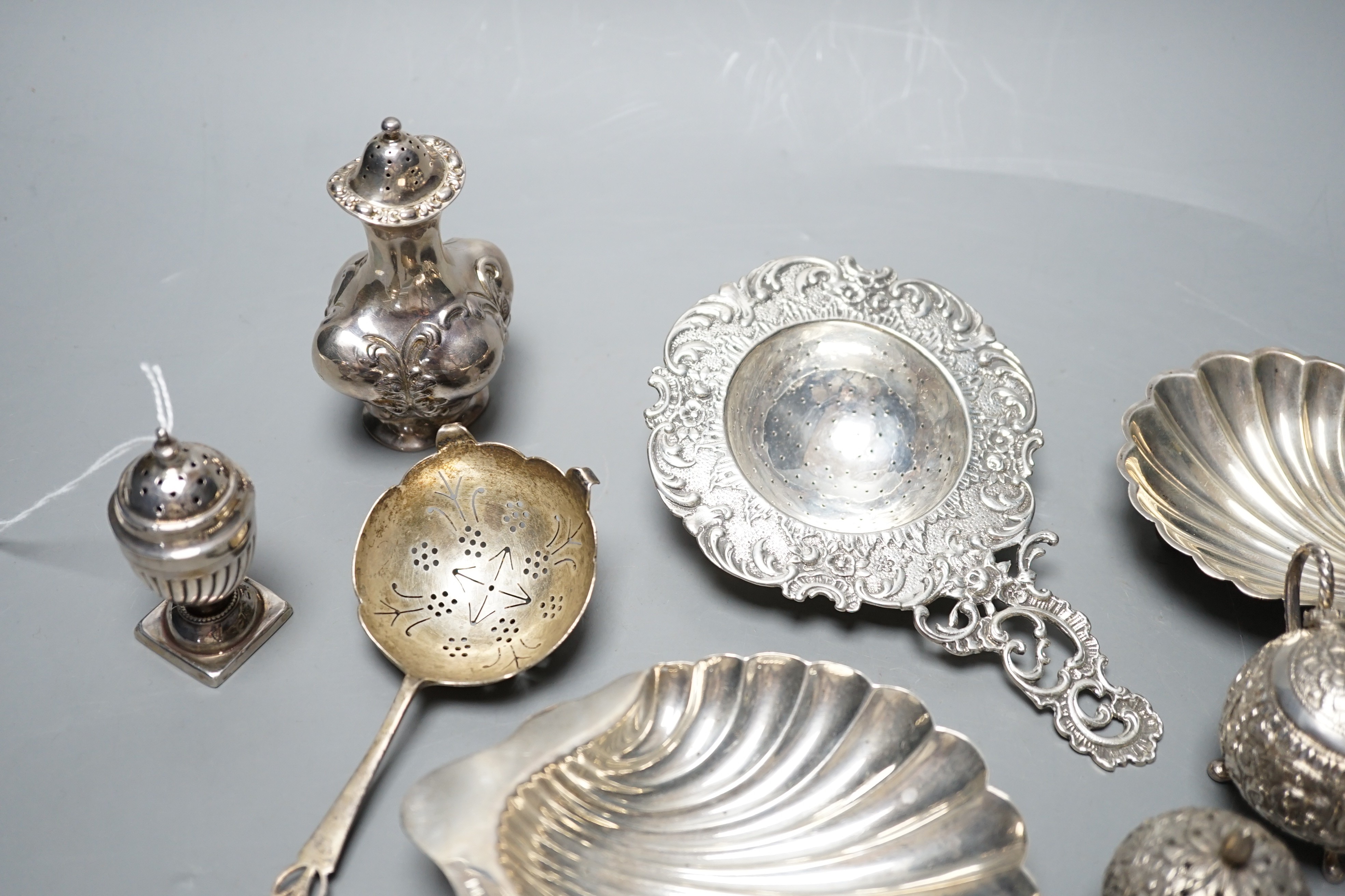 Small silver including two butter shells, a continental silver tea strainer, English tea strainer, pair of salts, swizzle stick, serving fork, two pepperettes and an Indian white metal three piece condiment set.